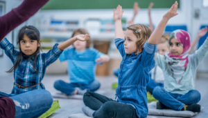 Photo of children doing yoga while seated on the floor with eyes open